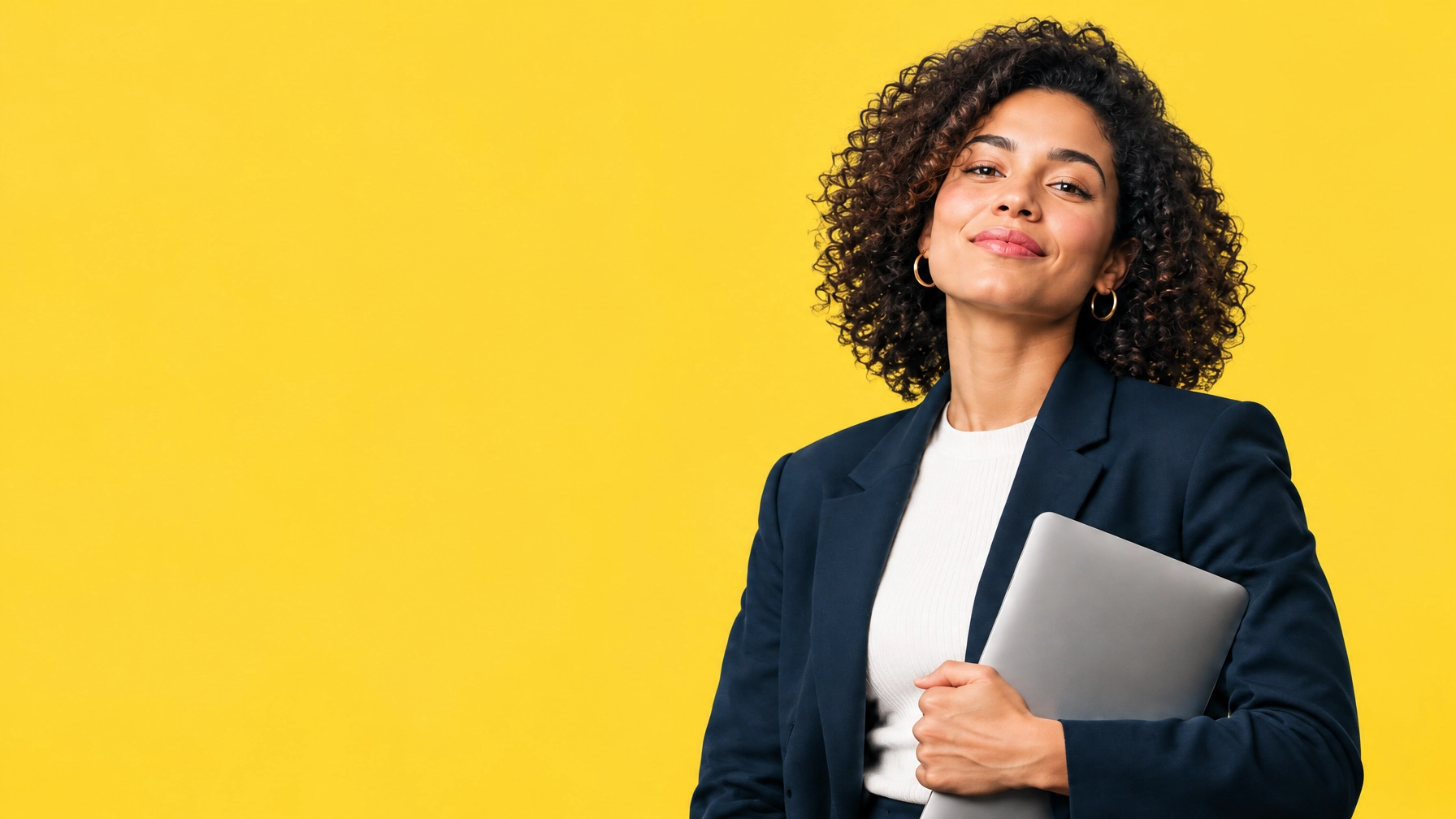 A smiling person in a navy blazer holding a laptop, against a yellow background.